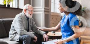 African nurse in uniform talking during day visit to old patient grandfather. Caring caregiver hold hand of 80s senior elderly man people having pleasant conversation, satisfied grandfather receiving support and care from carer concept