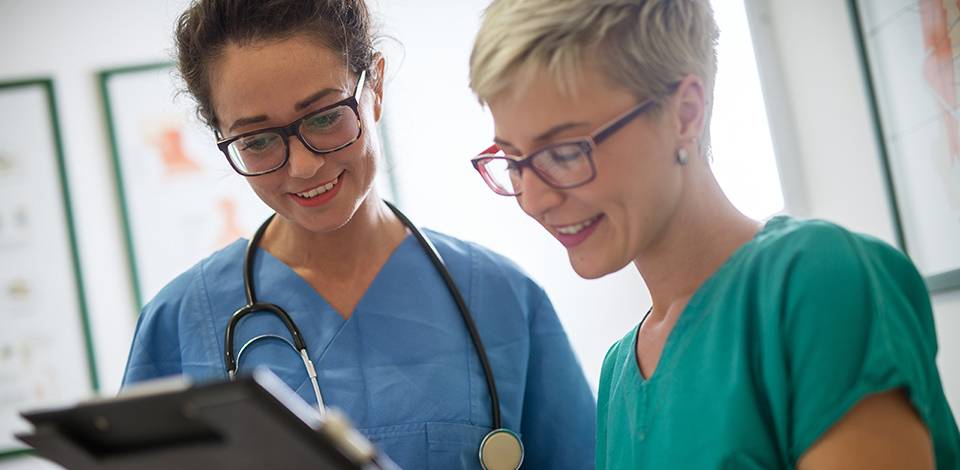 Close up of a two cheerful smiling professional female doctors with stethoscope looking at the clipboard of a patient.
